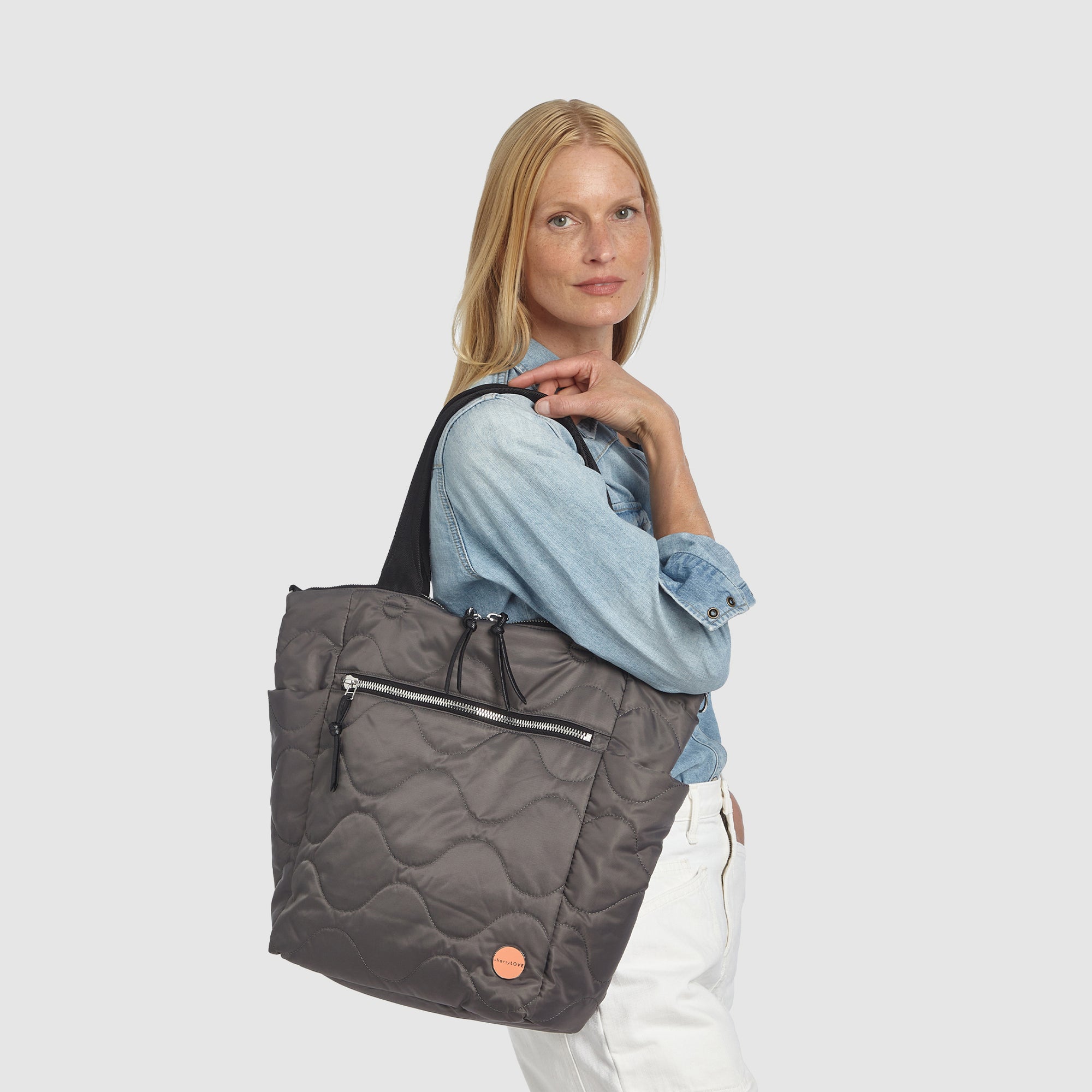 Woman in blue top and white jeans holding a pewter ranger quilted tote  bag on her shoulder