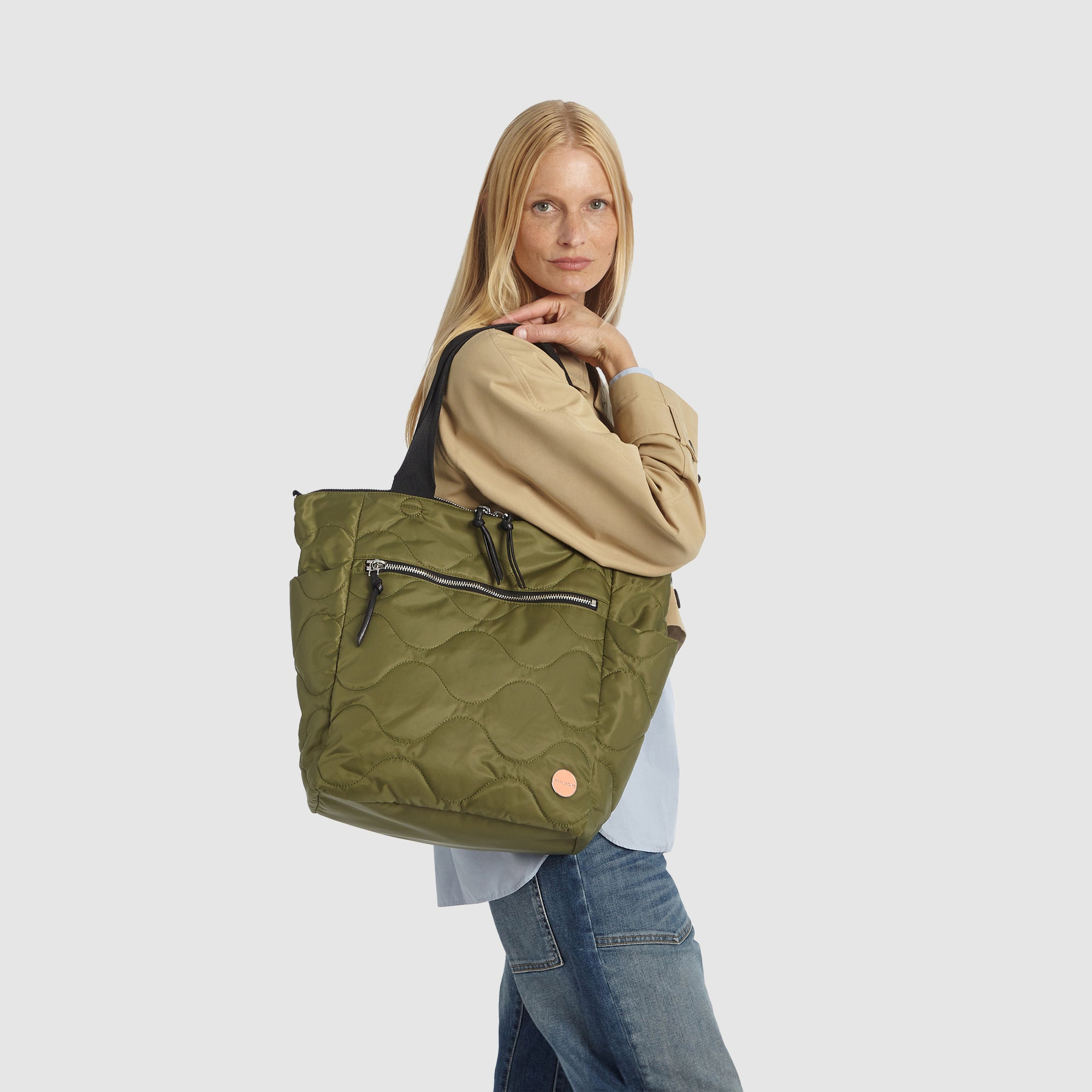 Person wearing a beige coat with a sage green quilted ranger tote bag over their shoulder on a white background