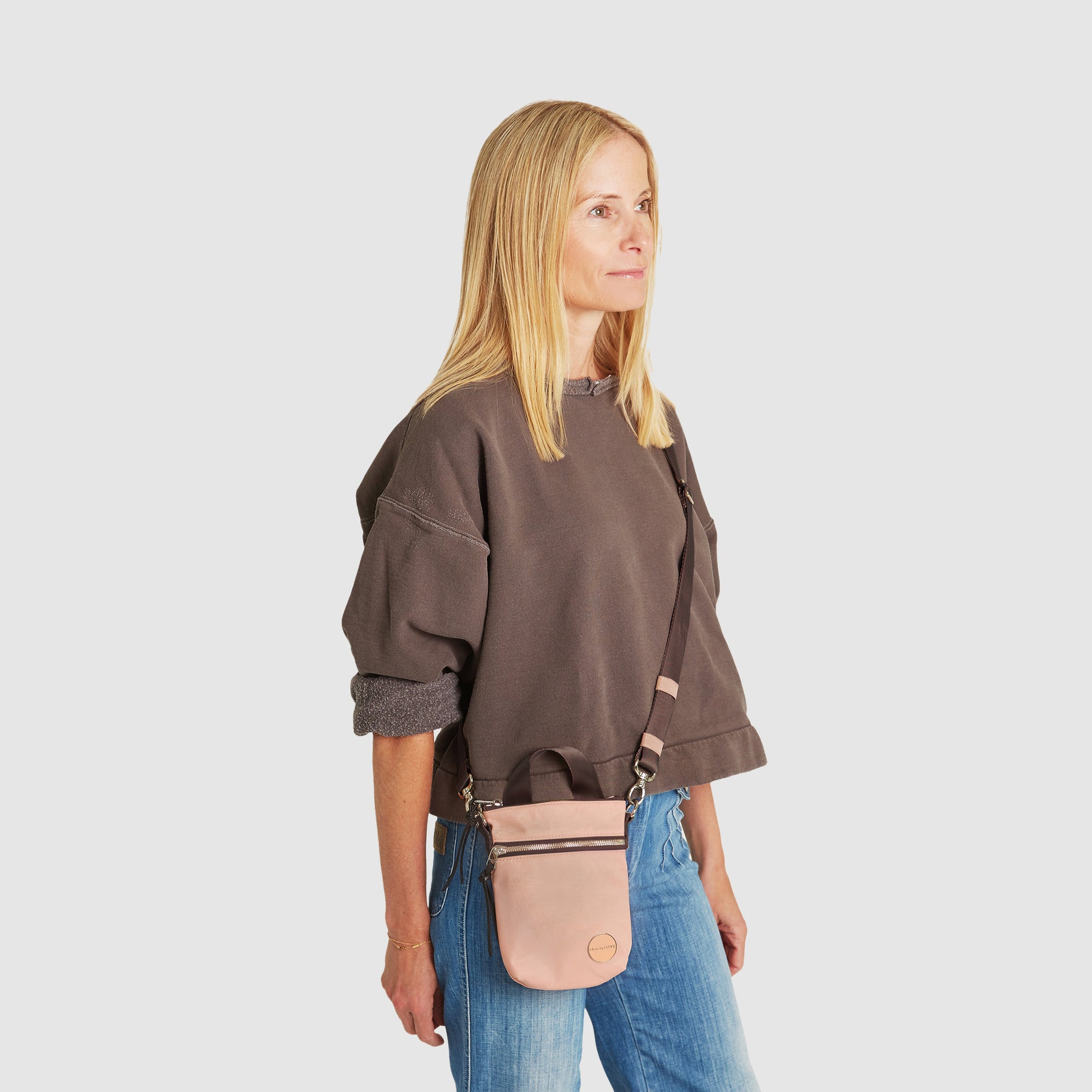 shortyLOVE shorthand small crossbody bag in dusty peach; on model in mocha sweatshirt and jeans against white background.