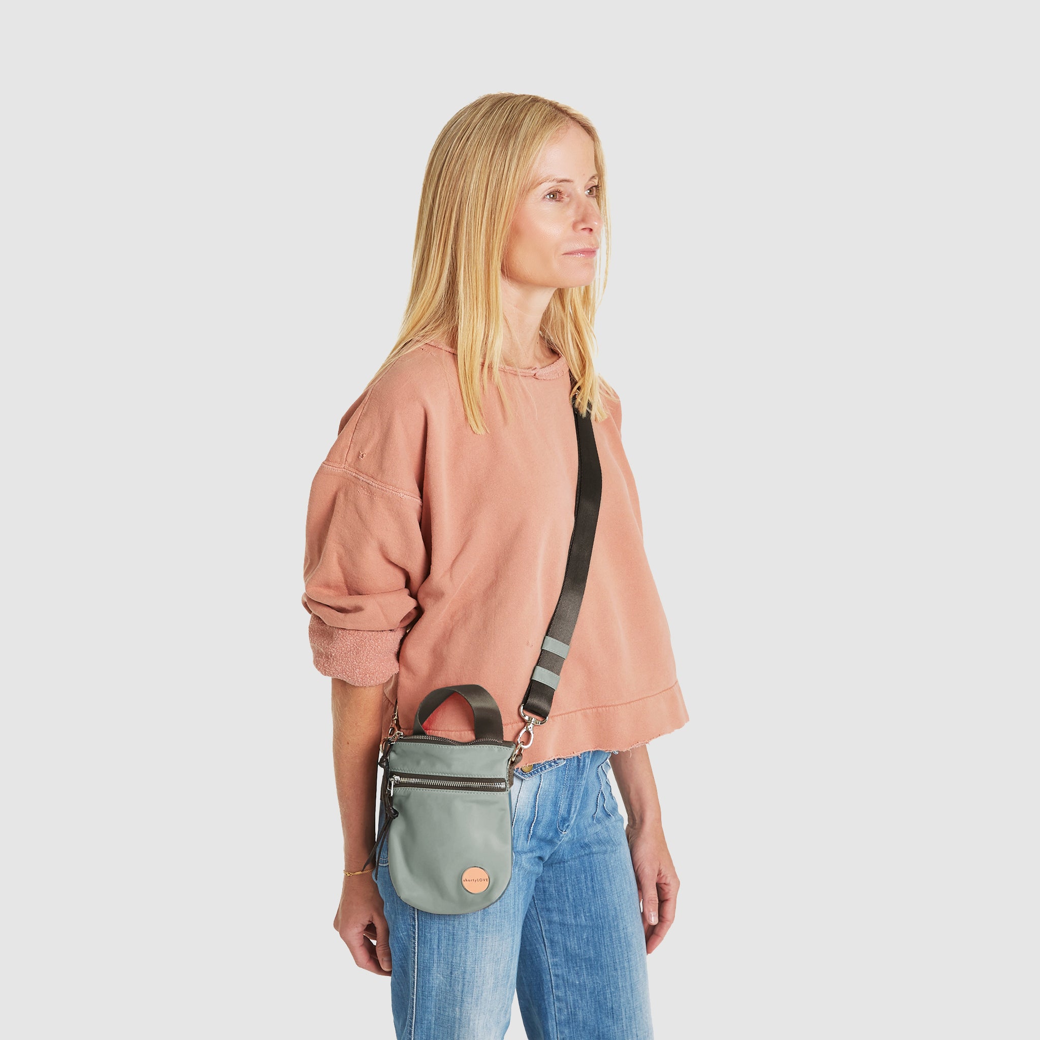 shortyLOVE shorthand small crossbody bag in slate/teal; on model in peach sweatshirt and jeans against white background.