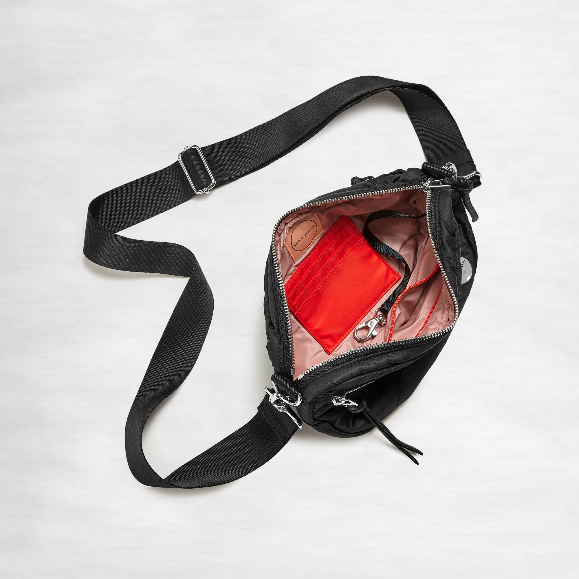 shortyLOVE small cruiser small crossbody bag in black; top-down view showing interior blush lining against white background.