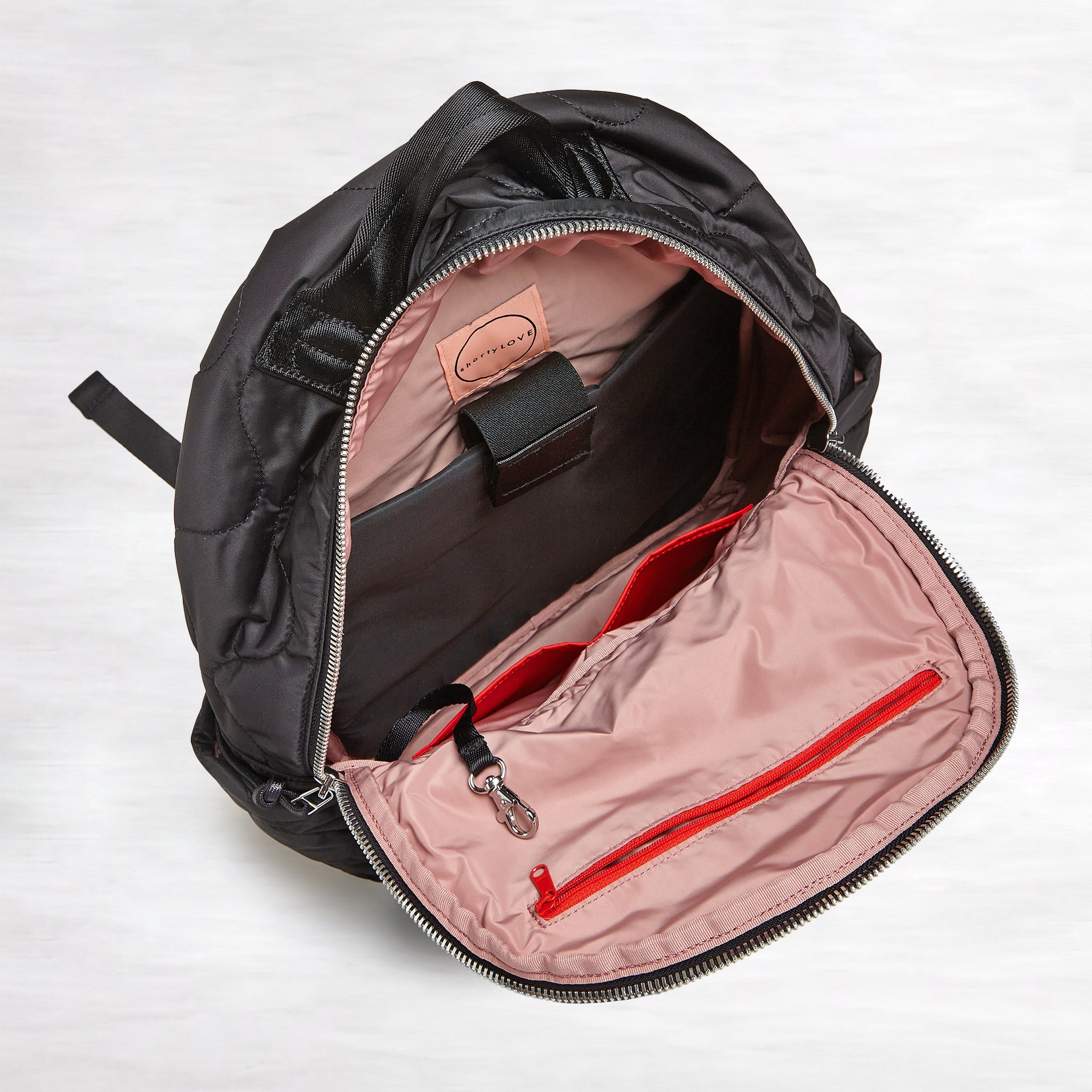 shortyLOVE tate backpack in black; top-down view showing interior blush lining against white background.