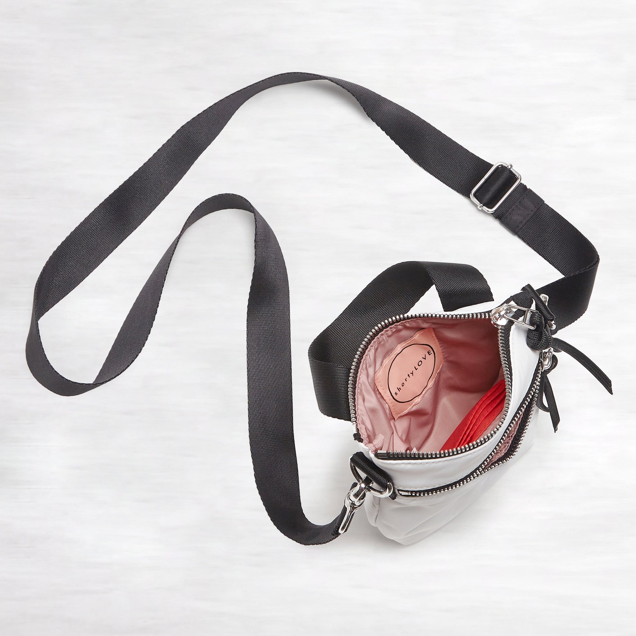 shortyLOVE shorthand small crossbody bag in white; top-down view showing interior blush/red lining against white background.