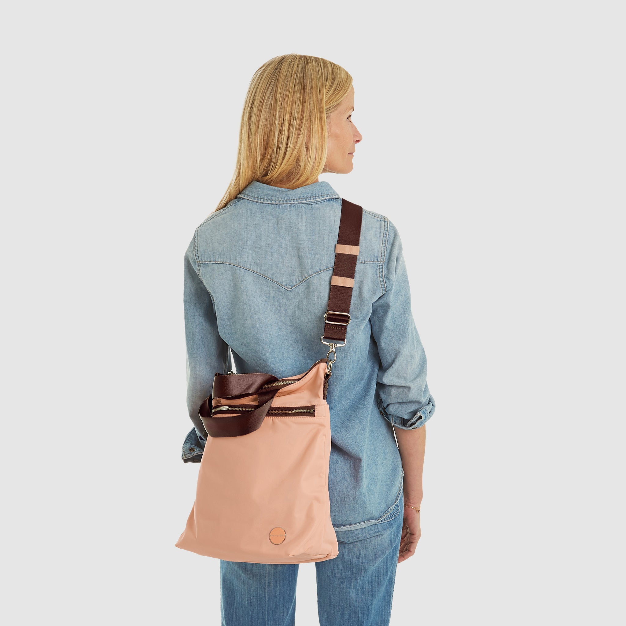 shortyLOVE wonder large crossbody/messenger bag in dusty peach; on model in jean top and jeans against white background.