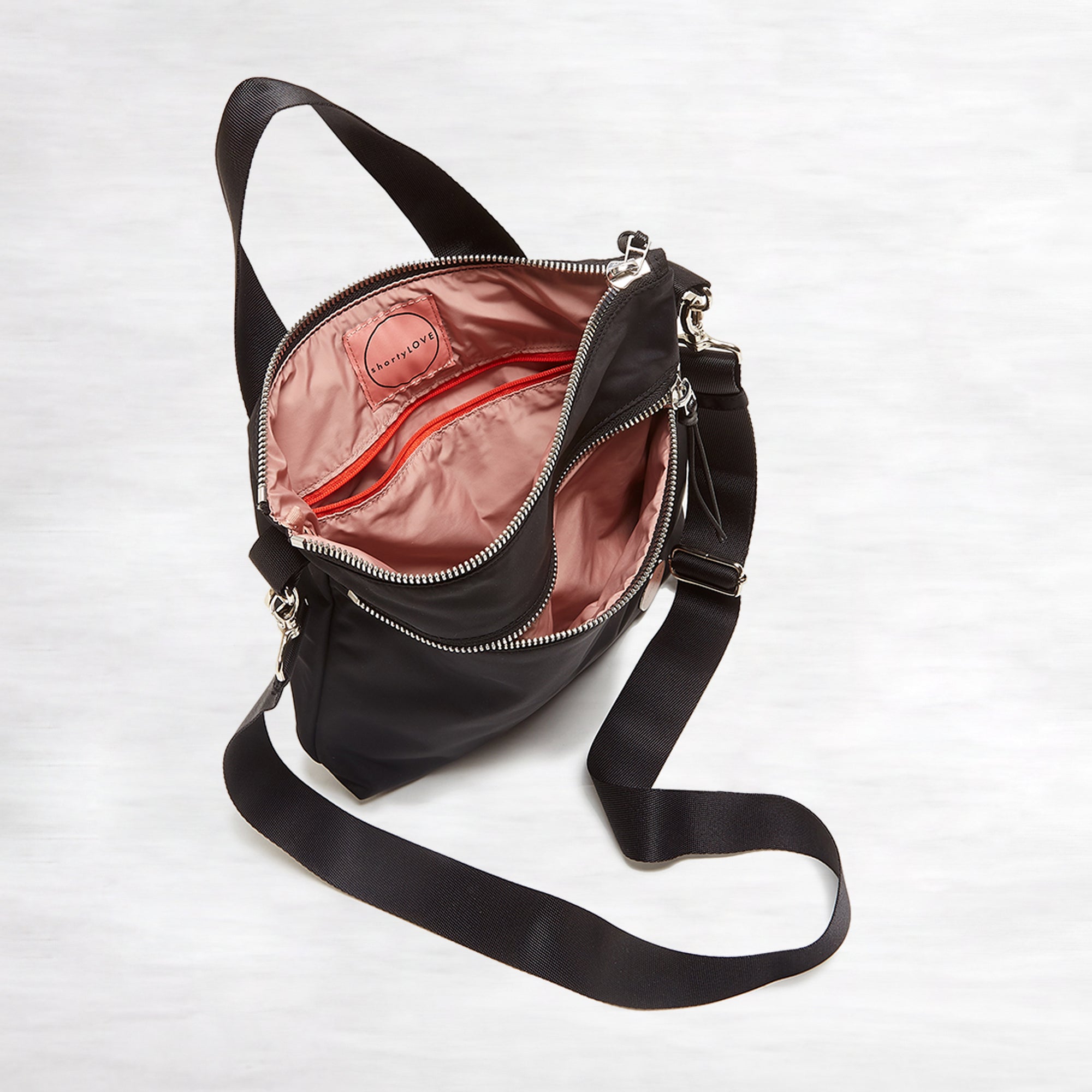 shortyLOVE amuse medium sized crossbody bag in black; top-down view showing interior pink lining against white background.