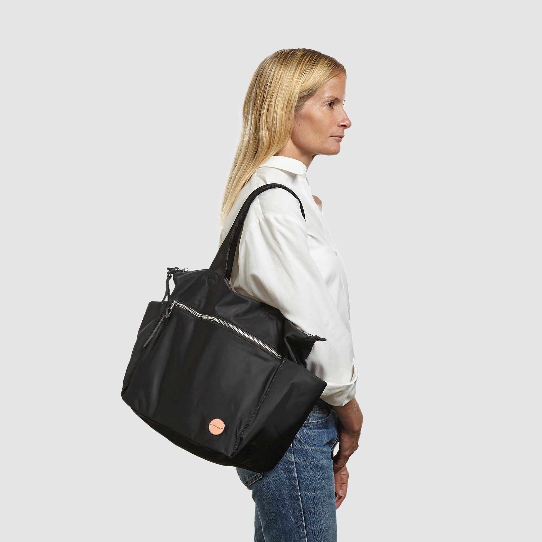 shortyLOVE tillie tote bag in black; on model in white button down shirt and jeans against white background.