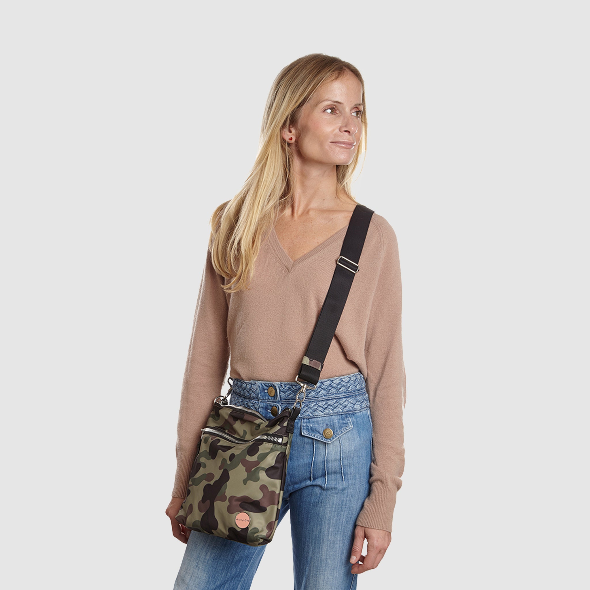 shortyLOVE amuse medium sized crossbody bag in green camo; on model in tan v-neck long sleeve sweater and jeans against white background.