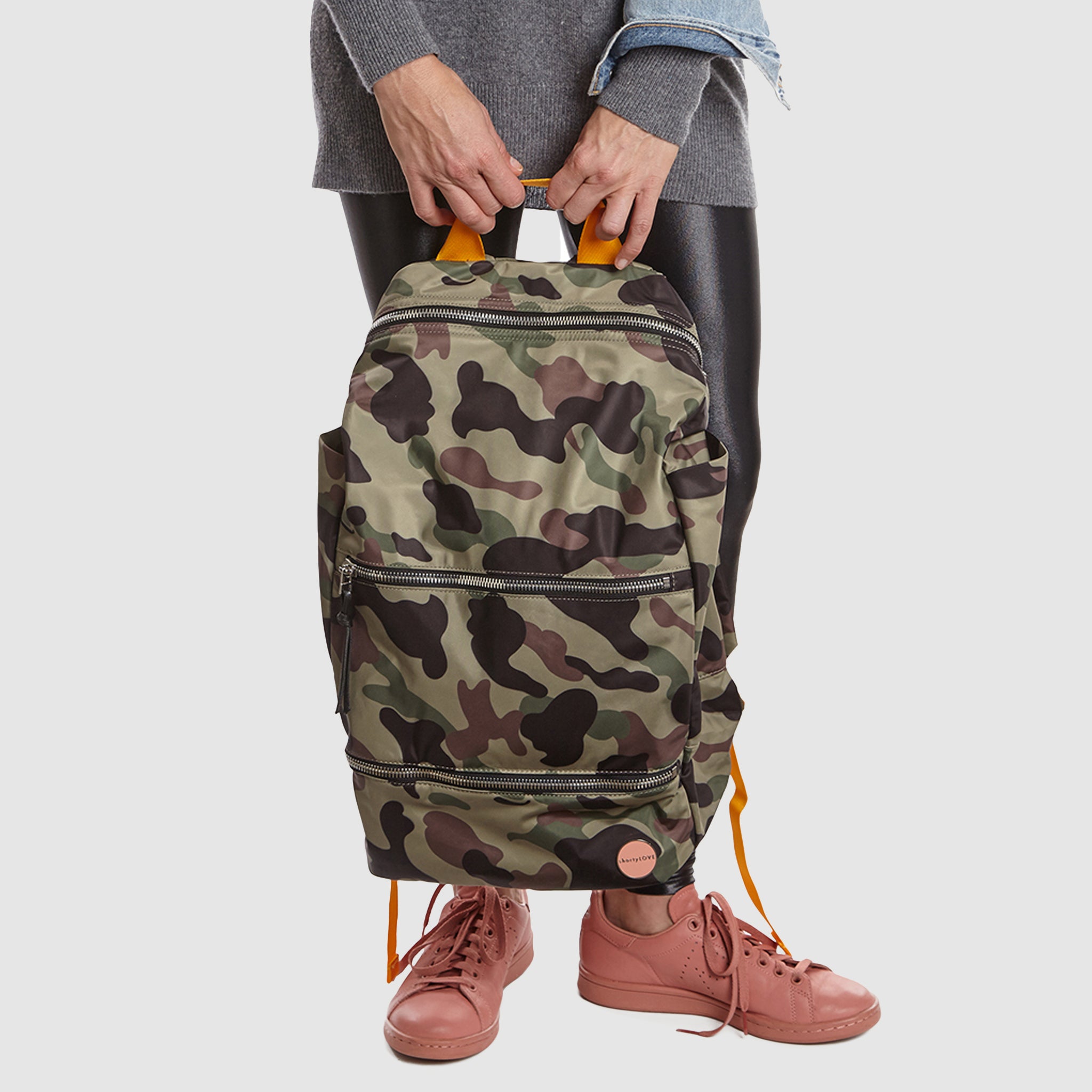 shortyLOVE boxer backpack bag in green camo; in hand of model in grey sweater and black leggings against white background.