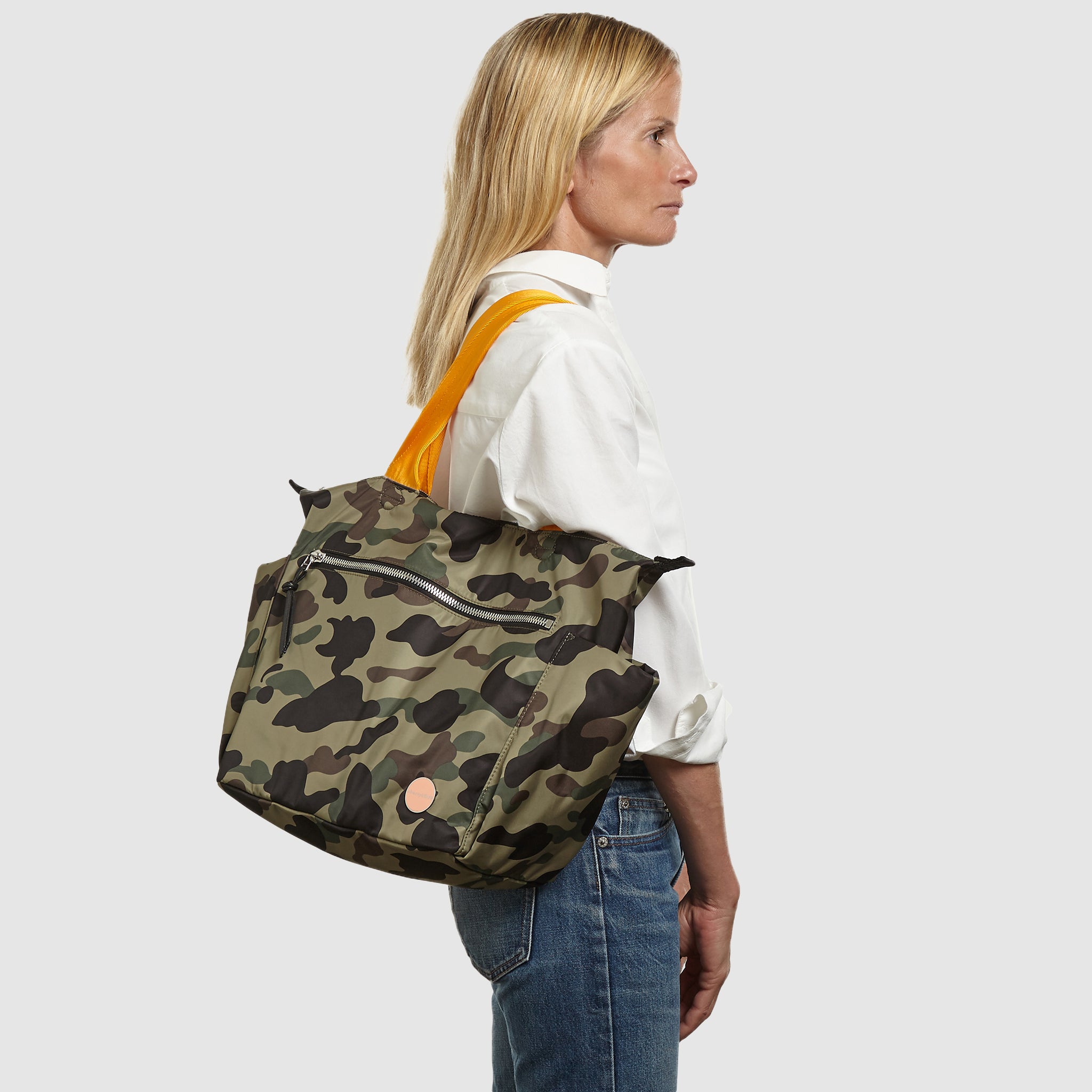 shortyLOVE tillie tote bag in green camo; on shoulder of model in white button down shirt and jeans against white background.