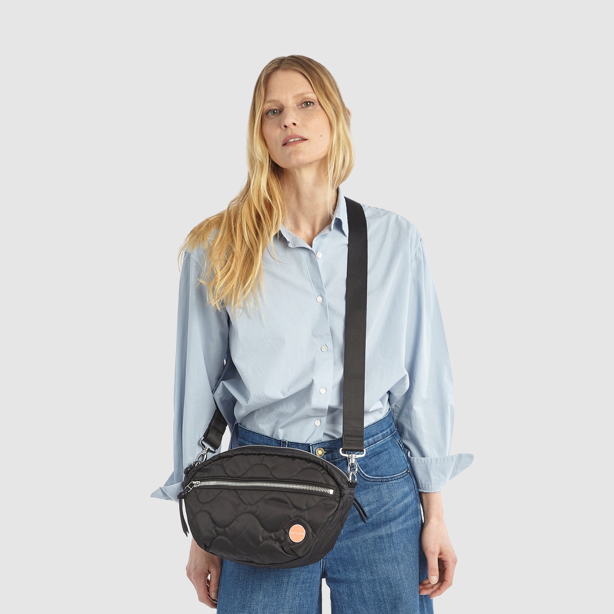 shortyLOVE cruiser medium crossbody bag in black; on model in blue button down shirt and jeans against white background.