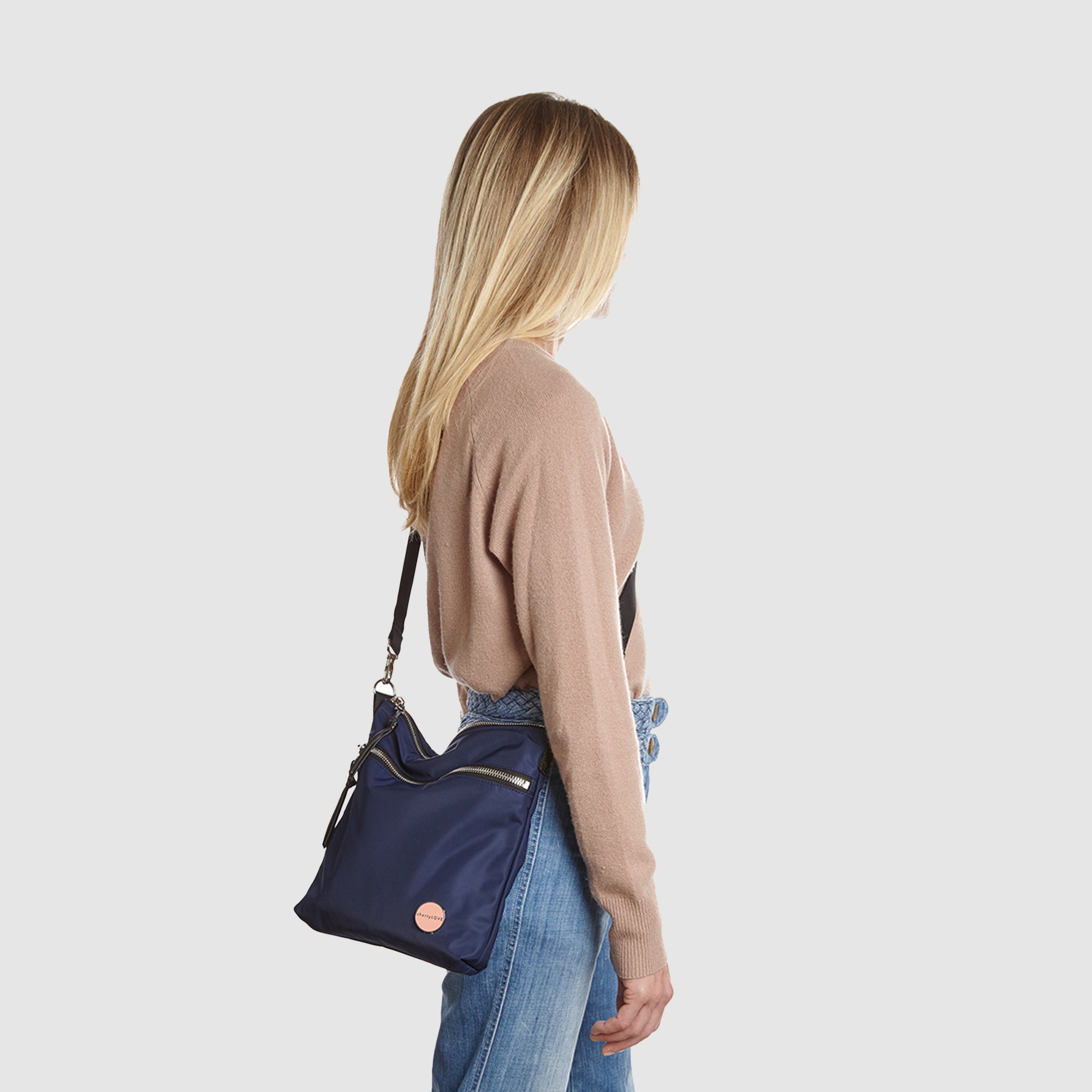 shortyLOVE amuse medium sized crossbody bag in navy; on model in tan v-neck long sleeve sweater and jeans against white background.