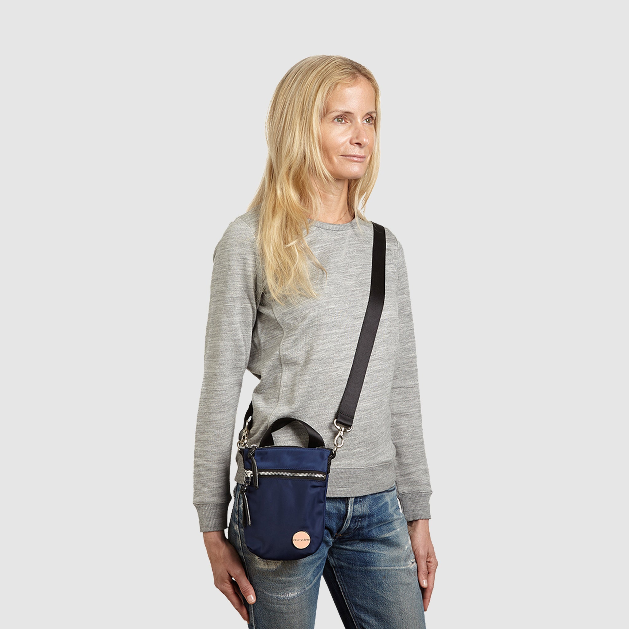 shortyLOVE shorthand crossbody phone bag in navy; on model in grey sweatshirt and jeans against white background.
