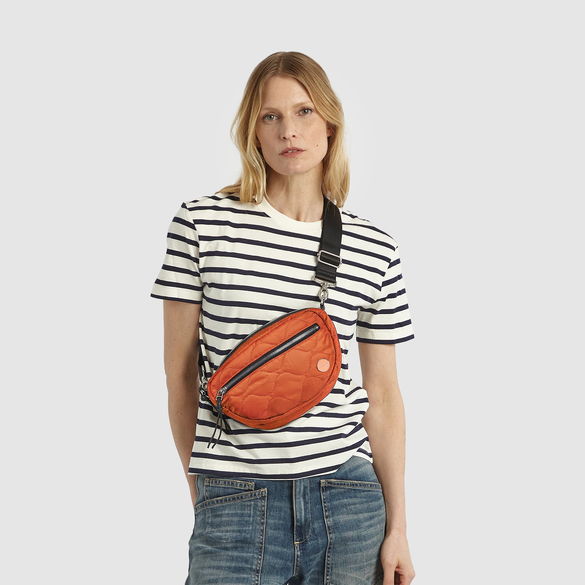 Model in striped tee short and jeans wearing an orange small cruiser crossbody bag