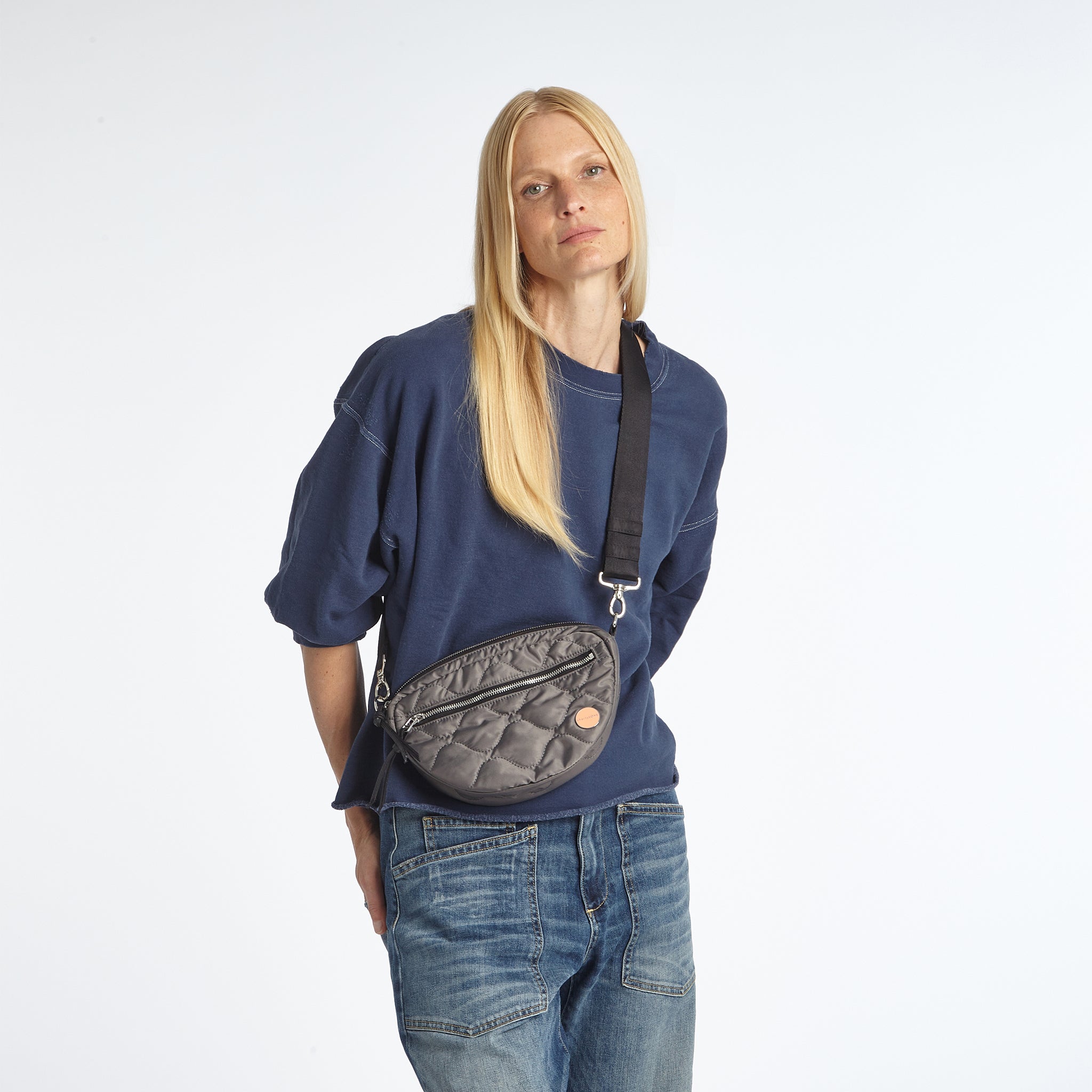 Model in navy sweatshirt and jeans wearing a pewter small cruiser crossbody bag 