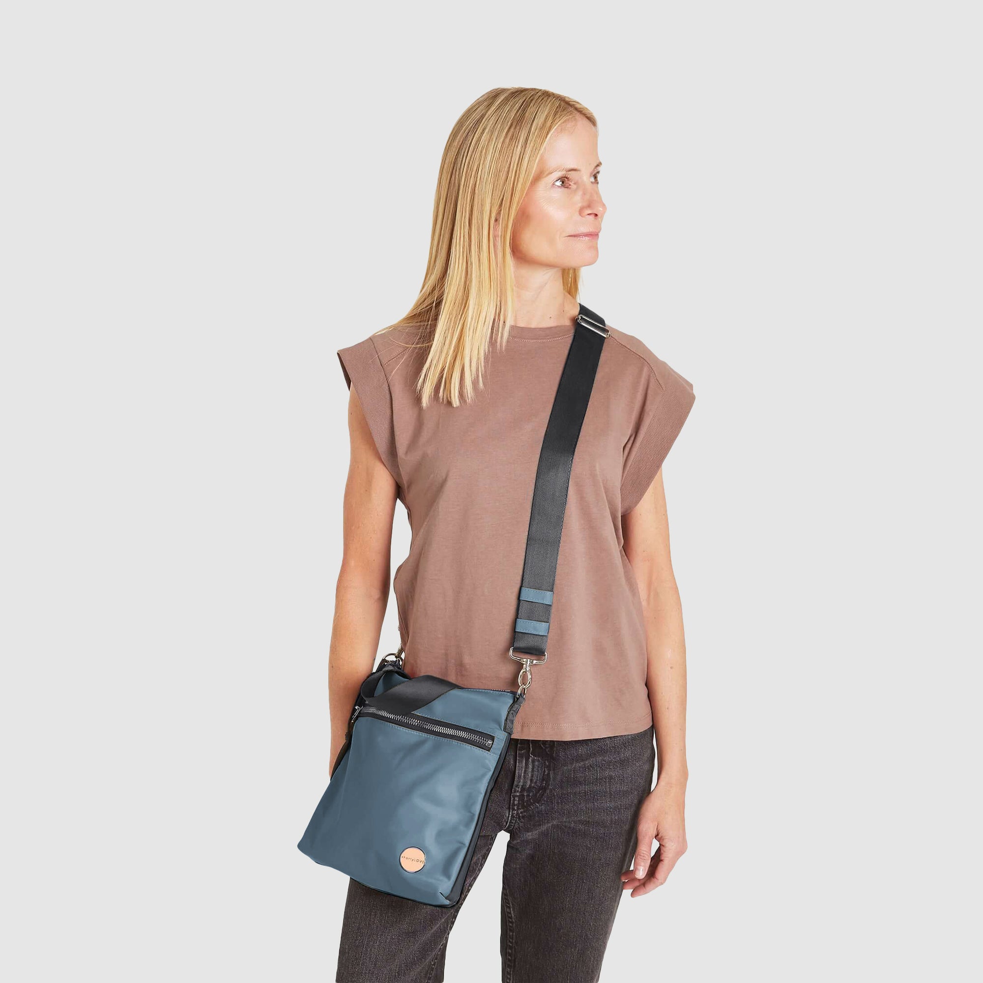 shortyLOVE amuse medium sized crossbody bag in steel blue/charcoal; on model in blush rose top and jeans against white background.