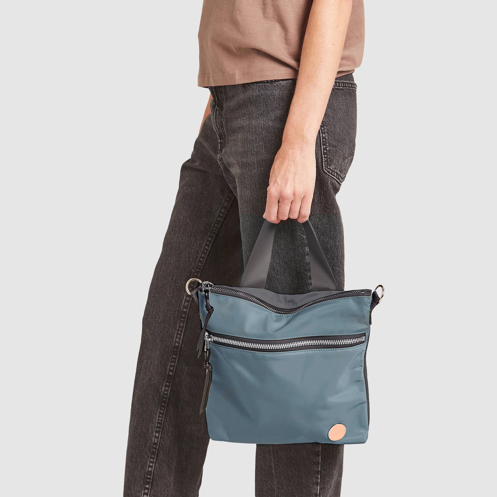 shortyLOVE amuse medium sized crossbody bag in steel blue/charcoal; on model in blush rose top and jeans against white background.