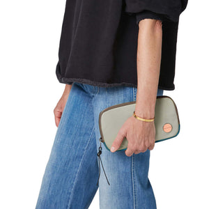 shortyLOVE jetty clutch/wallet in slate/teal; hand held by model in black sweatshirt and jeans against white background.