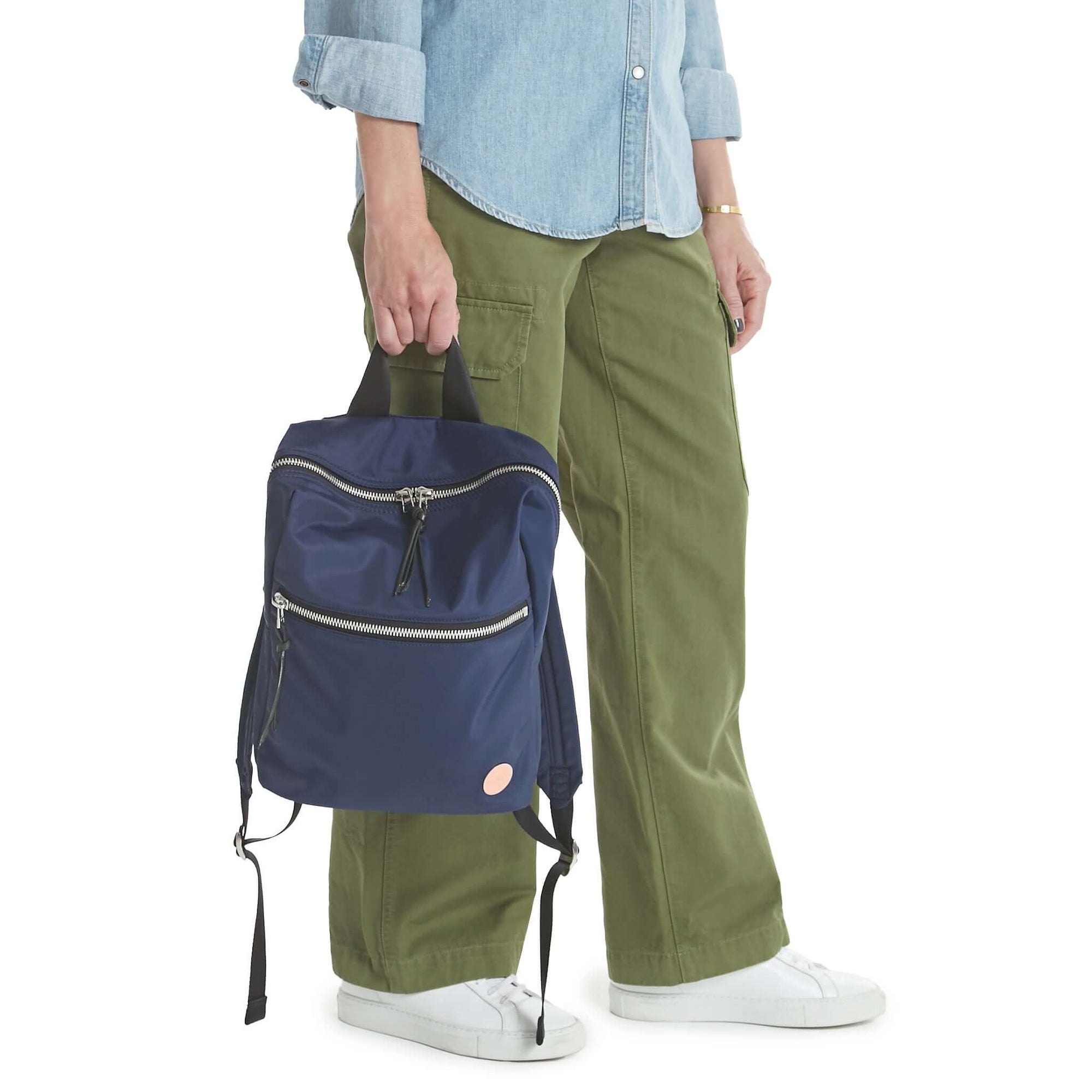 shortyLOVE ace small backpack in navy; hand held by modelin jean shirt and olive pants.