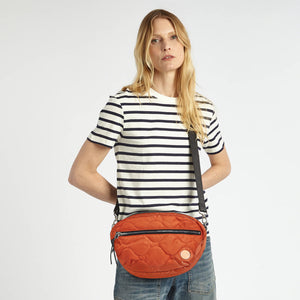 shortyLOVE cruiser medium crossbody bag in orange; on model in striped shirt and jeans against white background.