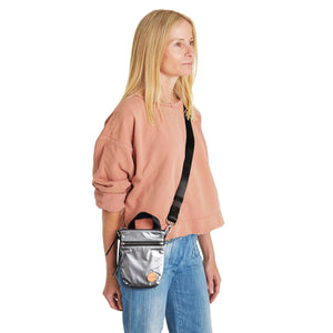 shortyLOVE shorthand small crossbody bag in silver; on model in peach sweatshirt and jeans against white background.