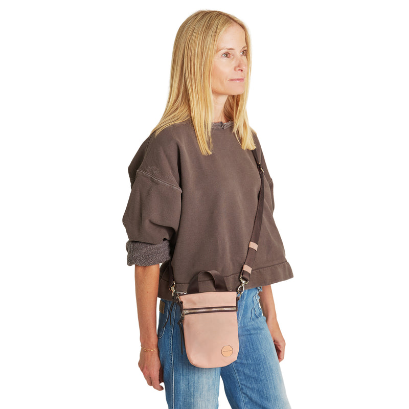 shortyLOVE shorthand small crossbody bag in dusty peach; on model in mocha sweatshirt and jeans against white background.