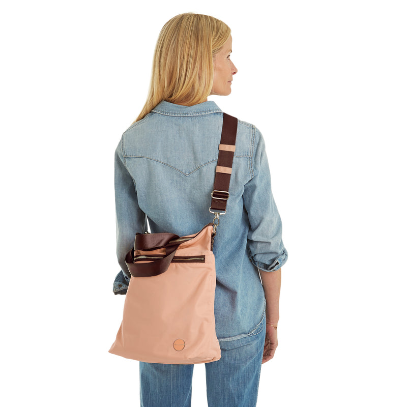 shortyLOVE wonder large crossbody/messenger bag in dusty peach; on model in jean top and jeans against white background.
