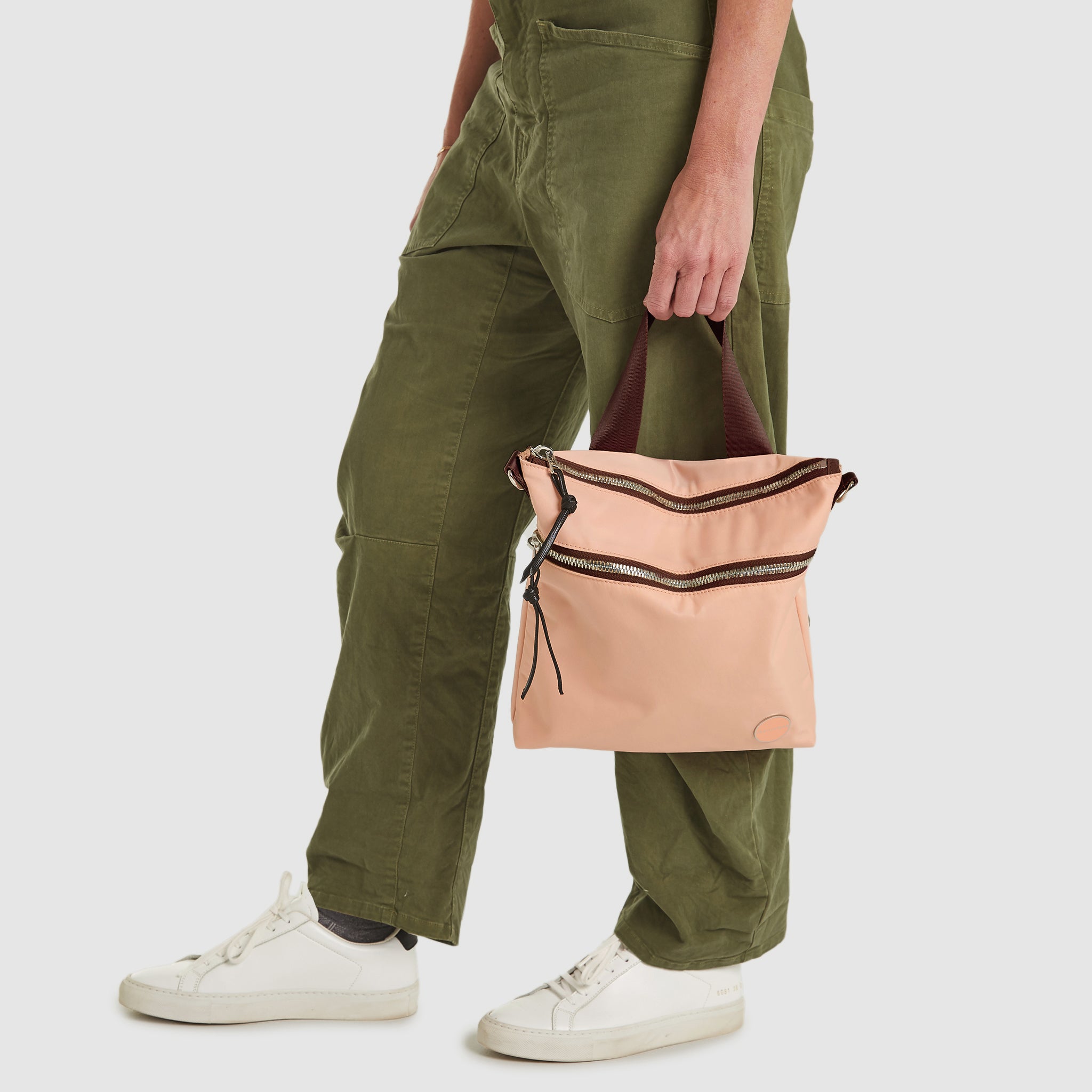 Woman holding a dusty peach amuse crossbody bag with a mocha strap against a white background