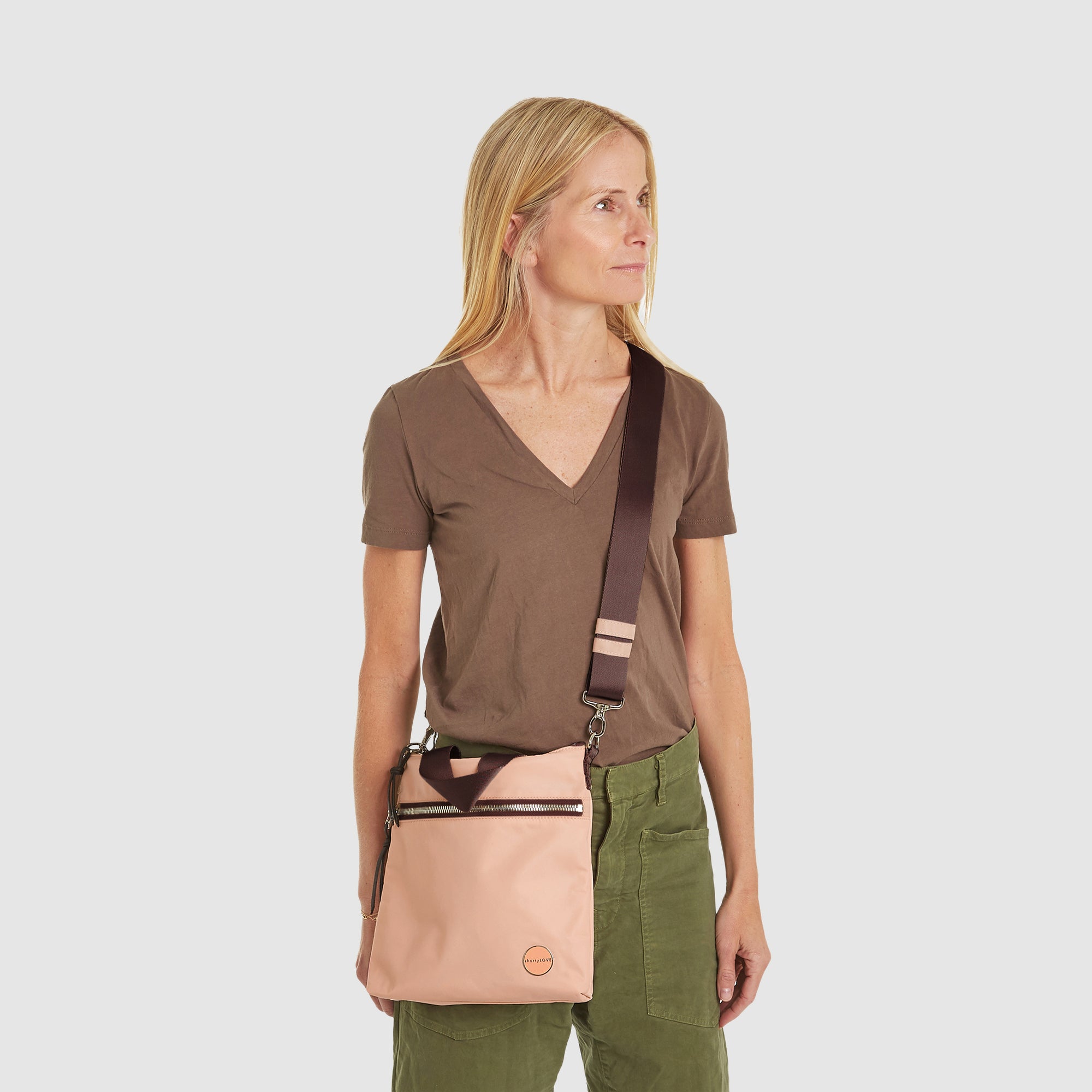 Woman holding a dusty peach amuse crossbody bag with a mocha strap against a white background