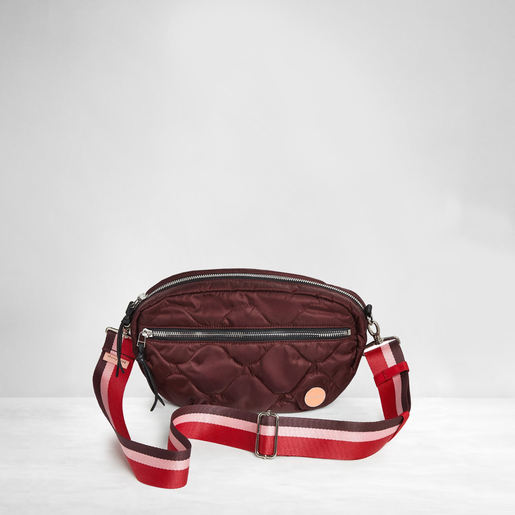 bordeaux small cruiser quilted crossbody bag with a burgundy/pink/red, striped strap on a light gray background