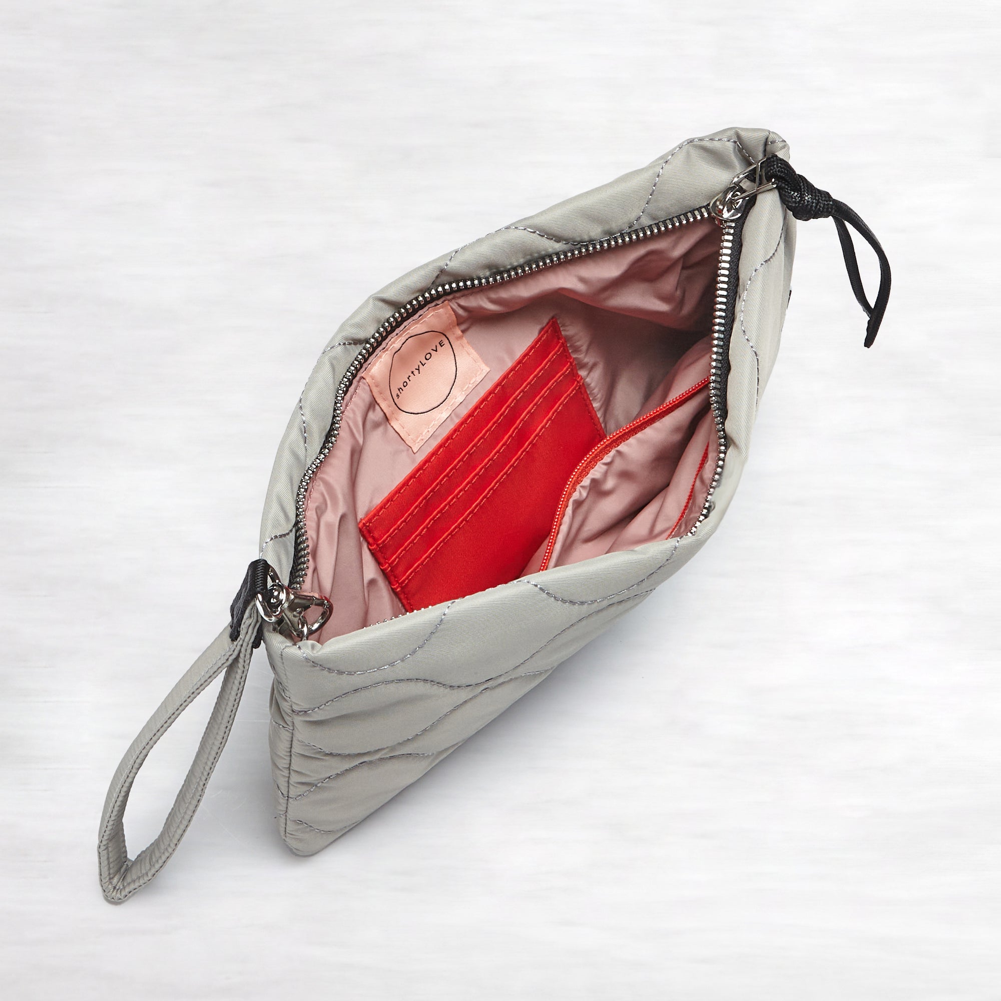 shortyLOVE cleo wristlet clutch in milky grey; top-down view showing interior blush lining against white background.