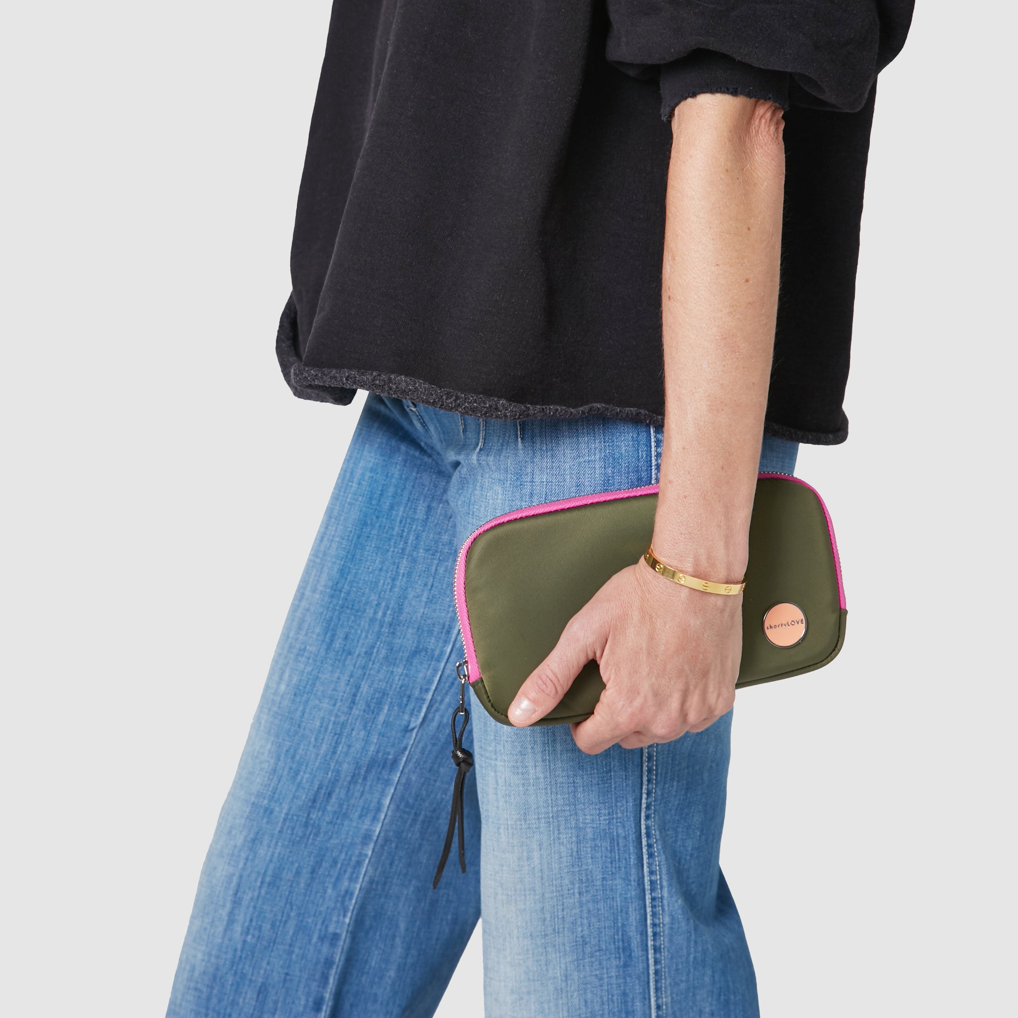 shortyLOVE jetty clutch/wallet in army green; hand held by model in black sweatshirt and jeans against white background.