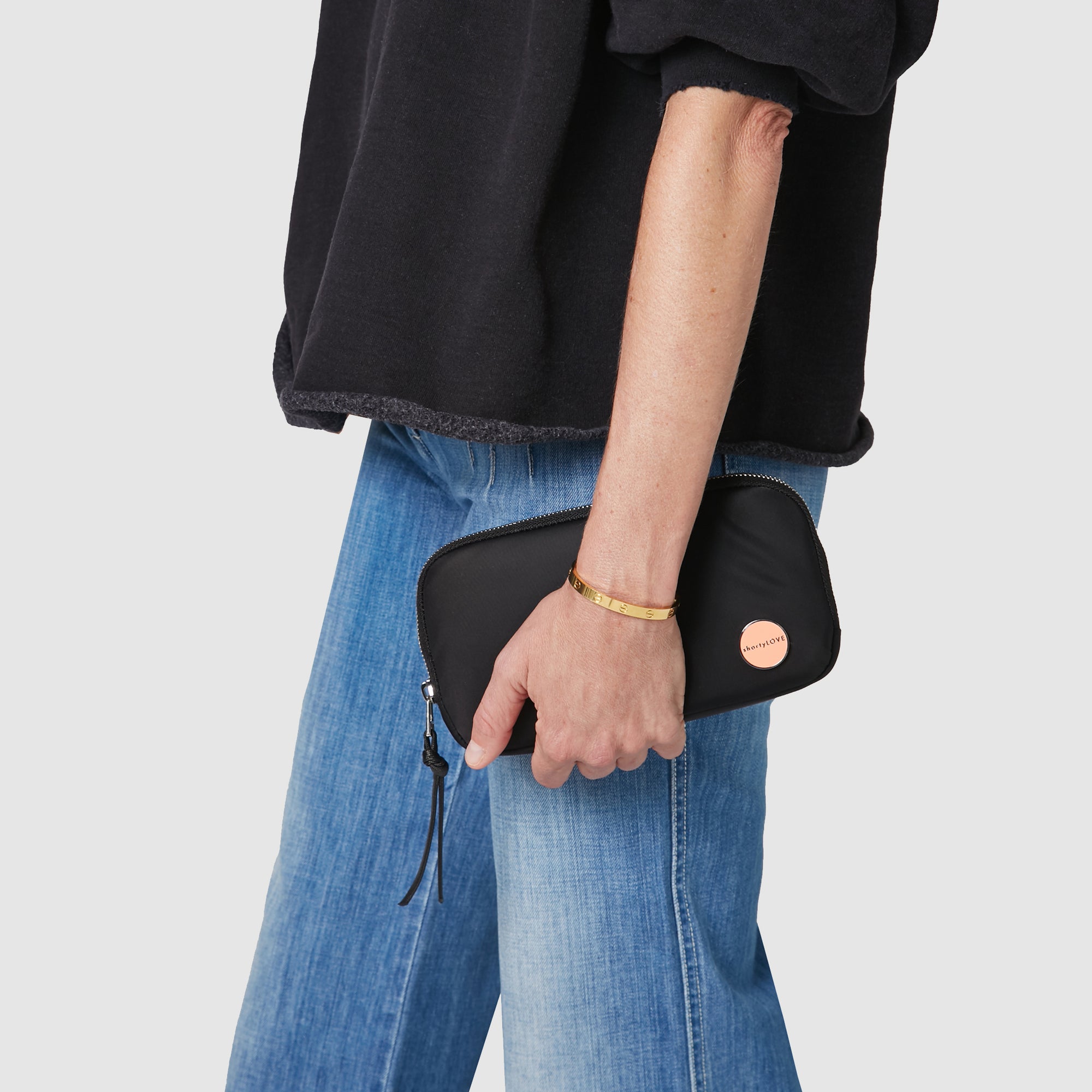 shortyLOVE jetty clutch/wallet in black; hand held by model in black sweatshirt and jeans against white background.