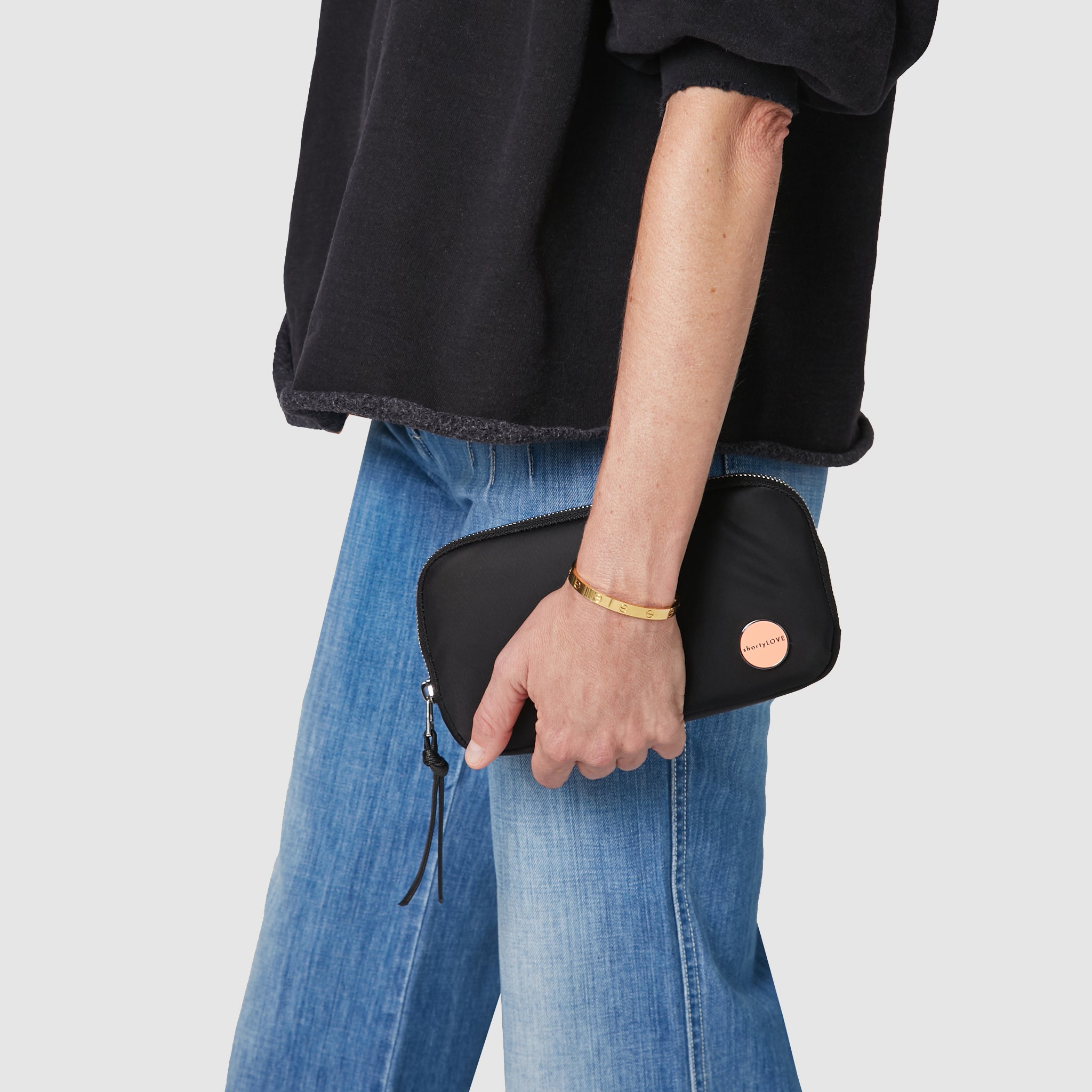 shortyLOVE jetty clutch/wallet in black; hand held by model in black sweatshirt and jeans against white background.
