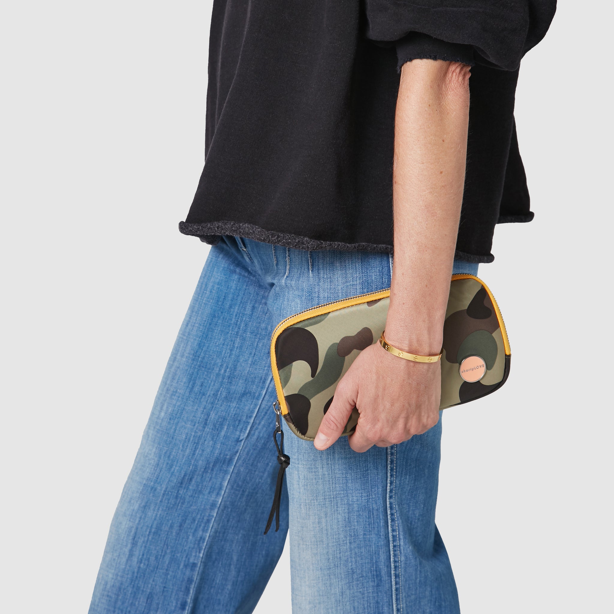 shortyLOVE jetty clutch/wallet in green camo; hand held by model in black sweatshirt and jeans against white background.