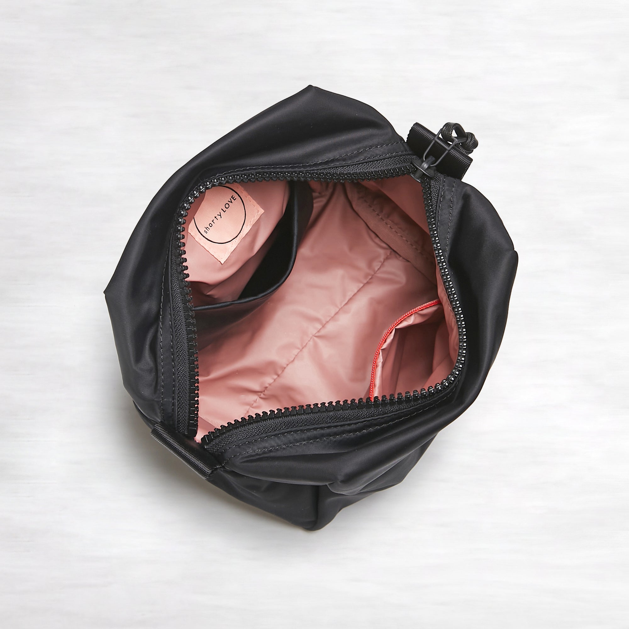 shortyLOVE stevie cosmetic bag in black; top-down view showing interior pink lining against white background.