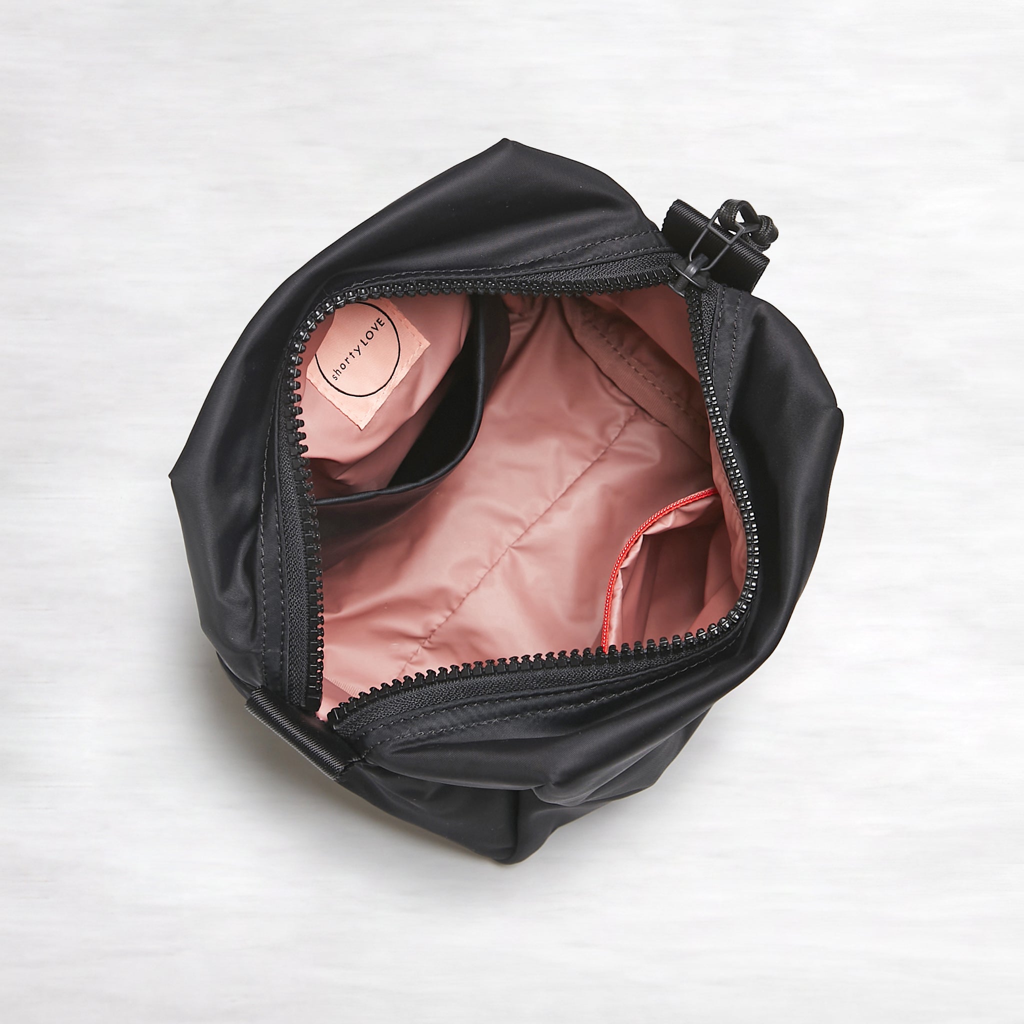 shortyLOVE stevie cosmetic bag in black; top-down view showing interior pink lining against white background.