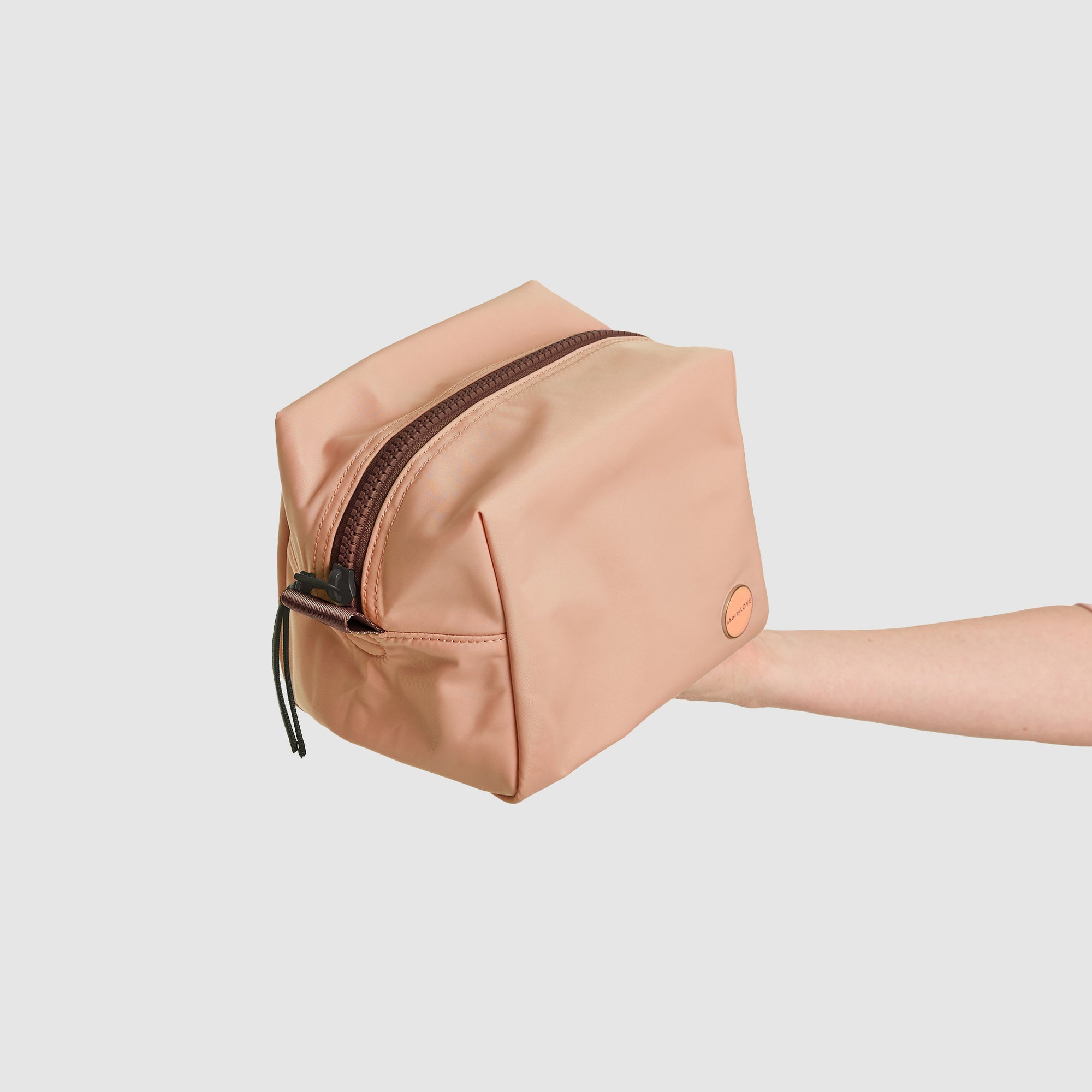 shortyLOVE stevie cosmetic bag in dusty peach; hand held by model against white background.