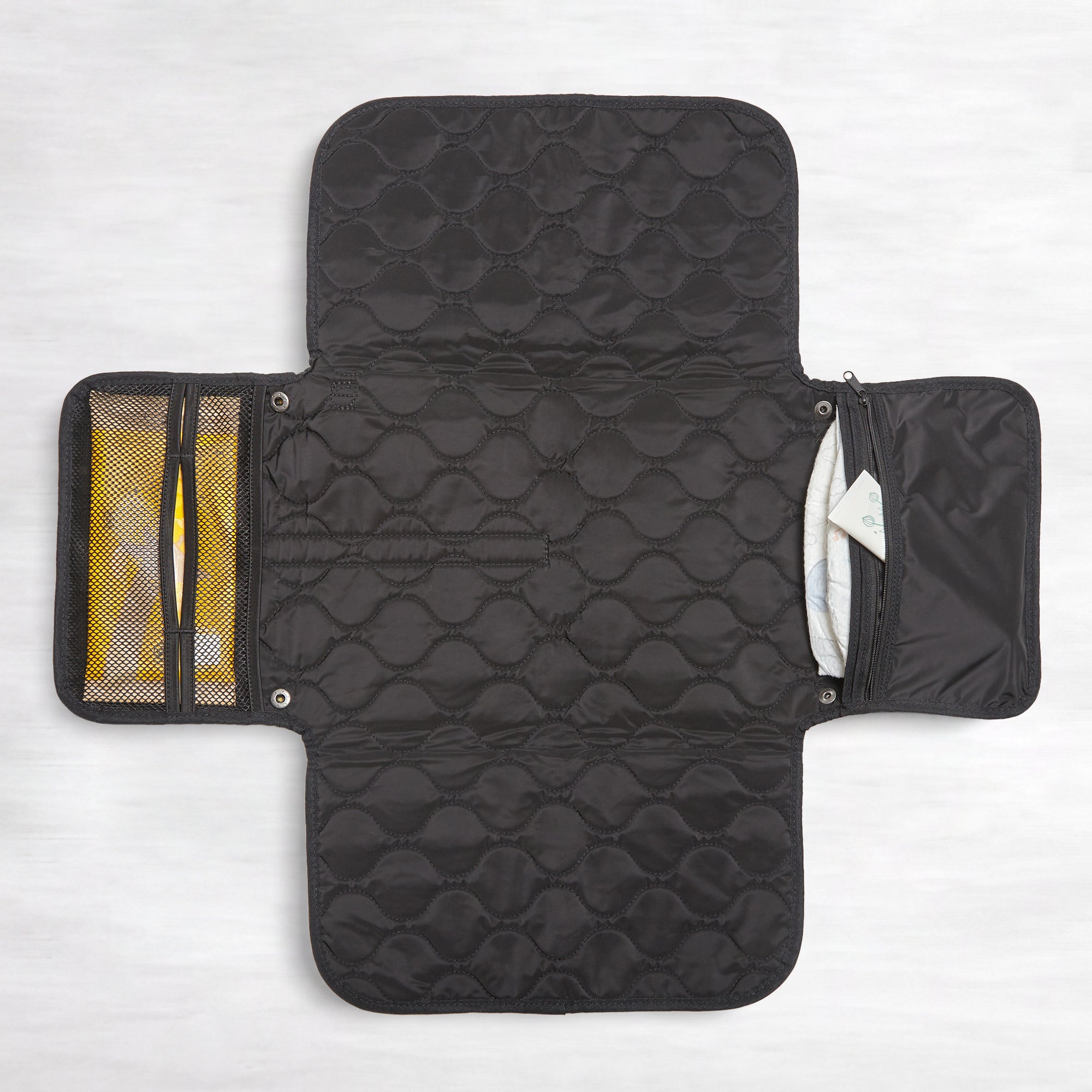 Black quilted diaper changing mat with multiple compartments on a white background