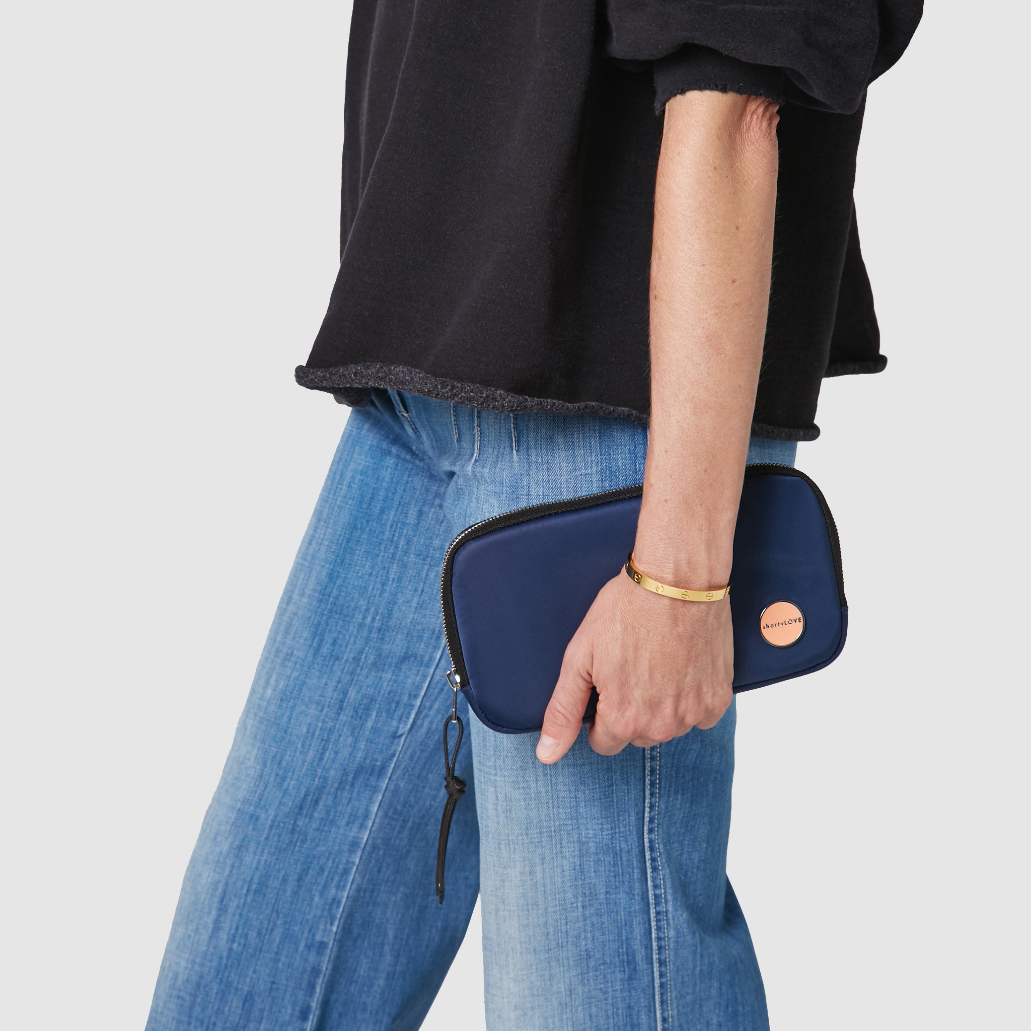 shortyLOVE jetty clutch/wallet in navy; hand held by model in black sweatshirt and jeans against white background.