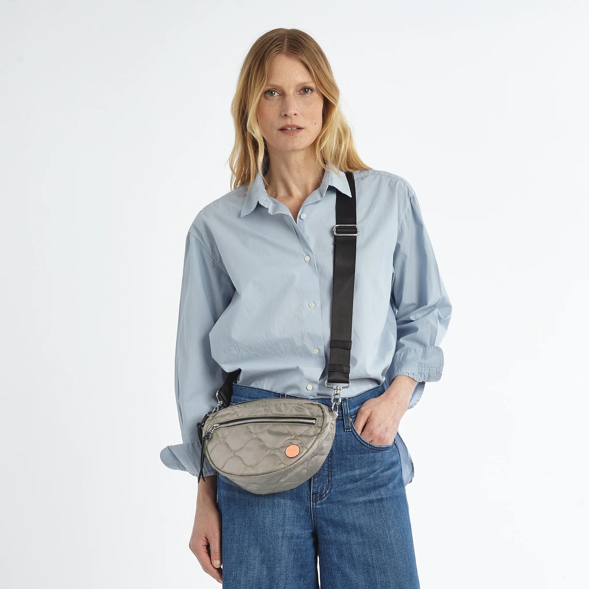 shortyLOVE small cruiser small crossbody bag in milky grey; on model in  blue shirt and jeans against white background.
