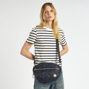 shortyLOVE cruiser medium crossbody bag in midnight; on model in striped blue and white shirt and jeans against white background.