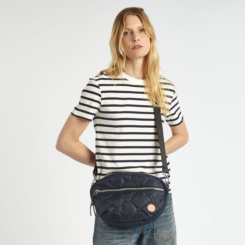 shortyLOVE cruiser medium crossbody bag in midnight; on model in striped blue and white shirt and jeans against white background.