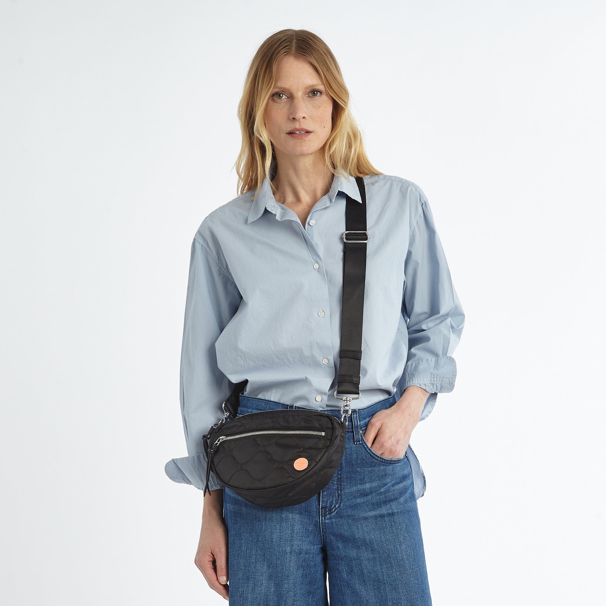 shortyLOVE small cruiser small crossbody bag in black; on model in blue button down shirt and jeans against white background.