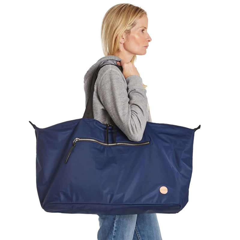 shortyLOVE friday weekender travel bag in navy; on model in grey hooded sweatshirt and jeans against white background.
