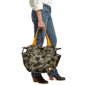 shortyLOVE tillie tote bag in green camo; hand held by model in white button down shirt and jeans against white background.