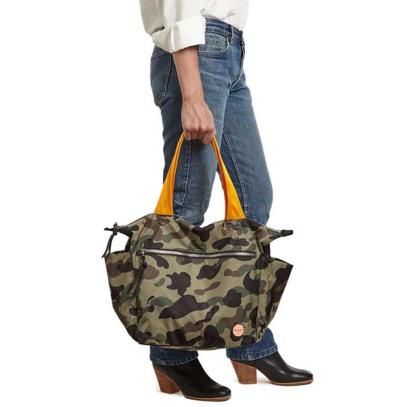shortyLOVE tillie tote bag in green camo; hand held by model in white button down shirt and jeans against white background.