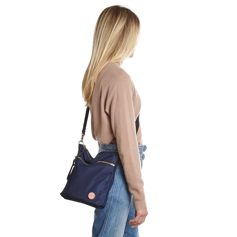 shortyLOVE amuse medium sized crossbody bag in navy; on model in tan v-neck long sleeve sweater and jeans against white background.