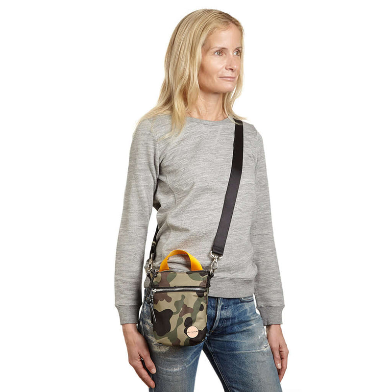 shortyLOVE shorthand crossbody phone bag in green camo; on model in grey sweatshirt and jeans against white background