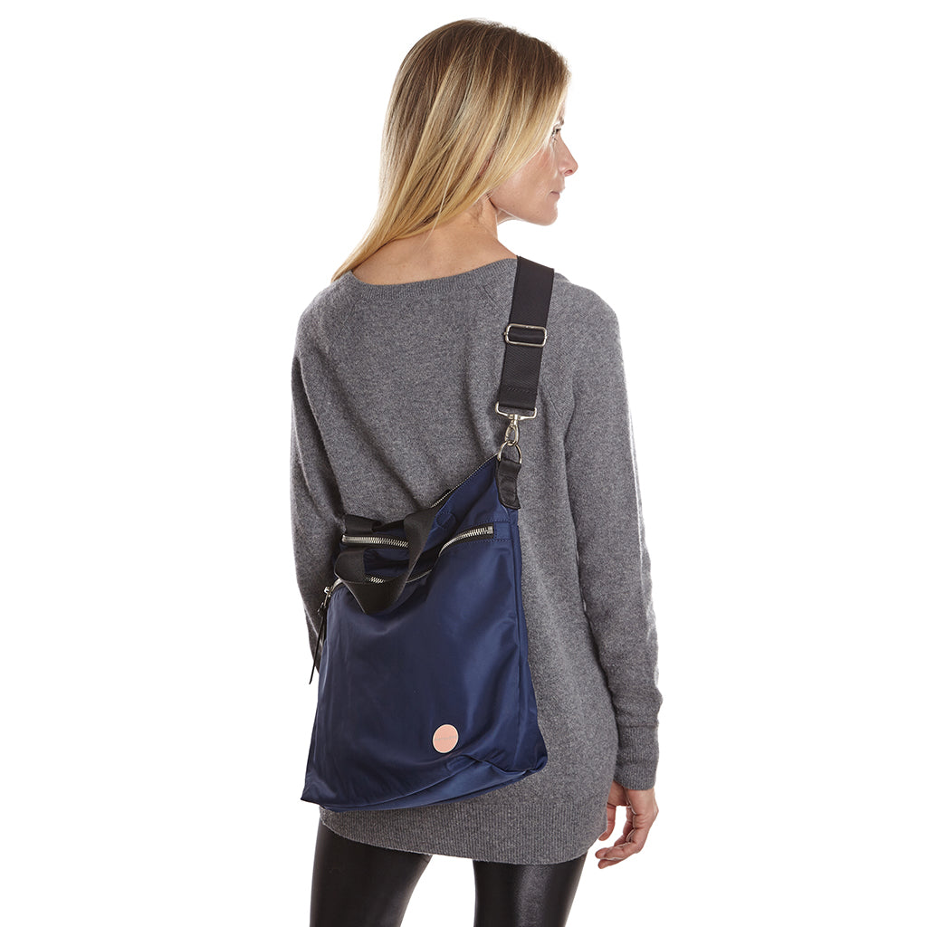 shortyLOVE wonder large crossbody/messenger bag in navy; on model in grey long sleeve sweater and black leggings against white background.