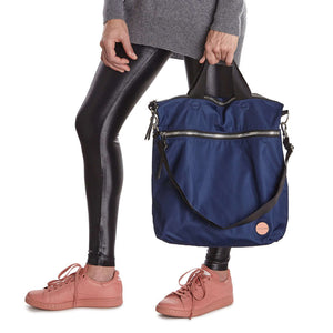 shortyLOVE wonder large crossbody/messenger bag in navy; hand held by model in grey long sleeve sweater and black leggings against white background.